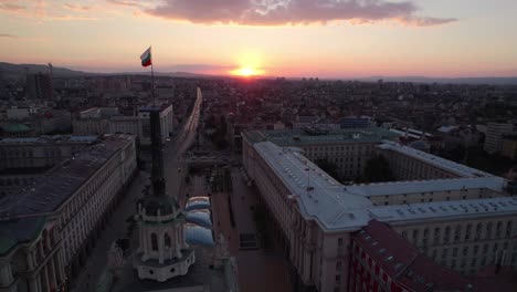 Sunset-aerial-drone-view-of-the-Bulgarian-Parliament-in-Sofia,-National-assembly-shows-Bulgarian-flag-over-skyline