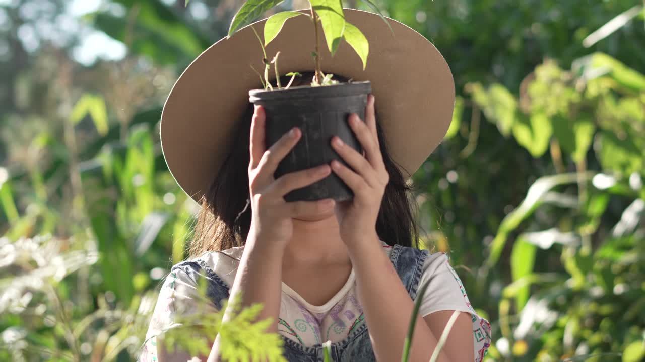 chica sonriente de pie en el medio de un jardín botánico con una planta de aguacate en sus manos