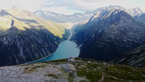 Un-Dron-Hacia-Abajo-Disparó-Una-Hermosa-Vista-Panorámica-De-La-Cabaña-Europea-Llamada-&quot;olpererhütte&quot;-En-Los-Alpes-Austriacos-En-Verano-Con-El-Schlegeis-Stausee-Debajo