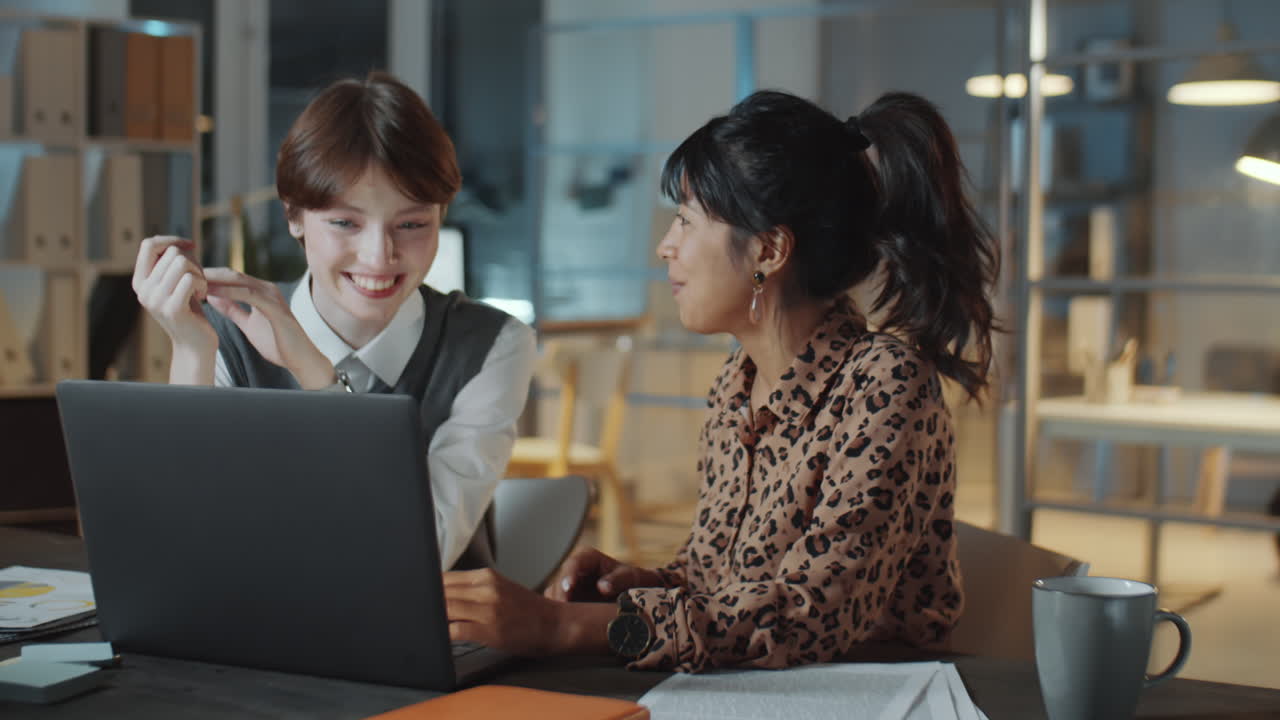 mujeres de negocios jóvenes discutiendo proyectos en computadora portátil en la oficina por la noche