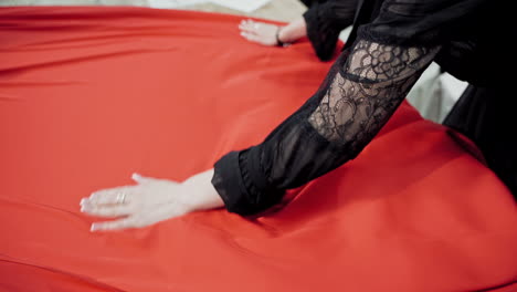 Professional tailor layng bright red fabric on a table. Work place table of sewer and a big piece of red cloth in workshop.