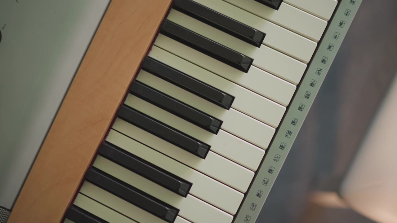 Tastiera vintage ripresa dall'alto con finiture in legno e controlli retrò, inquadratura diagonale; compositore che arrangia melodia e voicing degli accordi, estetica analogica, grana calda e tasti tattili, creatività da home studio