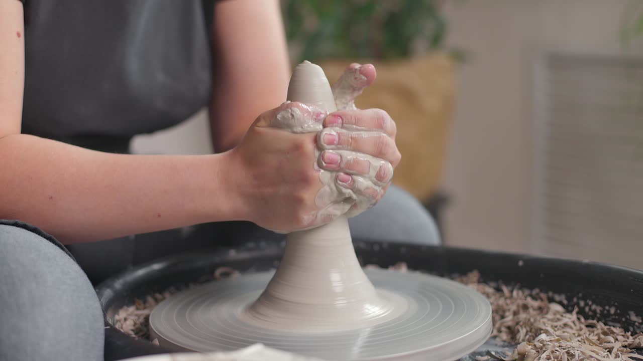 Närbild på handen av en mästerkrukmakare som arbetar vid en drejskiva och formar en skål av lera. Slow motion.