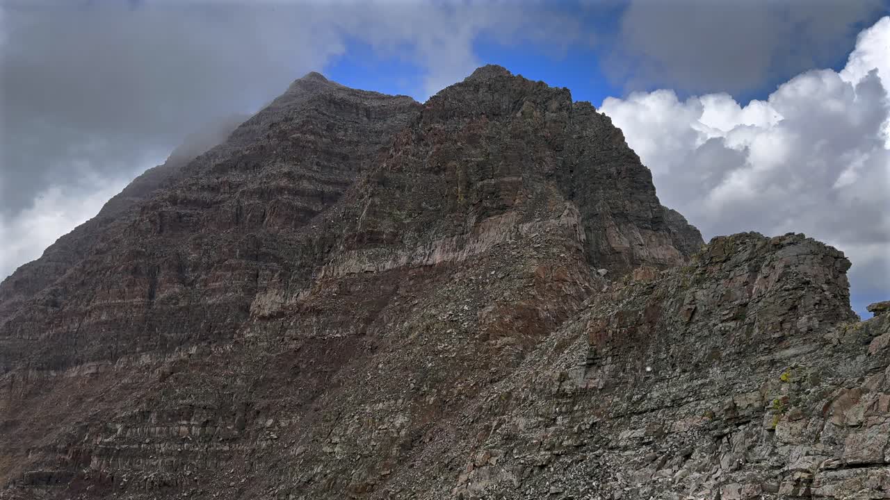 Maroon Peak snowing backside high elevation fourteener rugged mountain terrain Bells Wilderness Colorado sunny summer clouds fog movement Aspen Snowmass Elk Range Rocky Mountains static shot