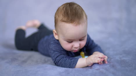 lovely toddler in blue clothes lying peacefully on the bed. cute child looks at pacifier with interest and then around himself.
