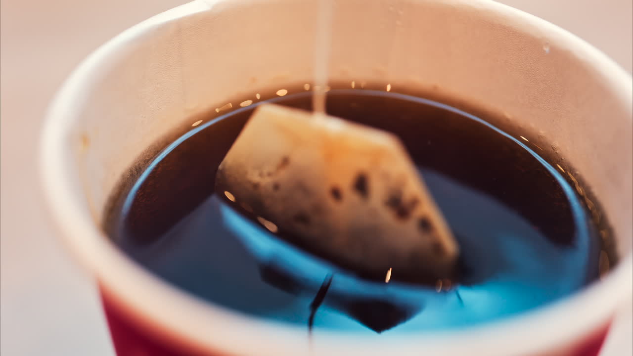 Close up of a tea bag brewing into a red cup