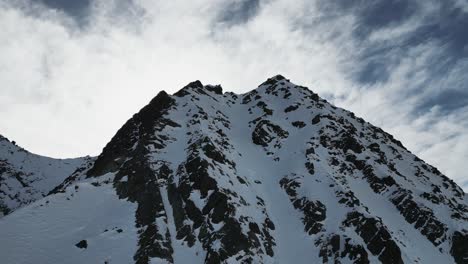 aerial steep snow icy mountain top slope flying towards snowy peak on sunny day, alpine landscape