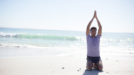 a young biracial man practices yoga on a sunny beach with copy space