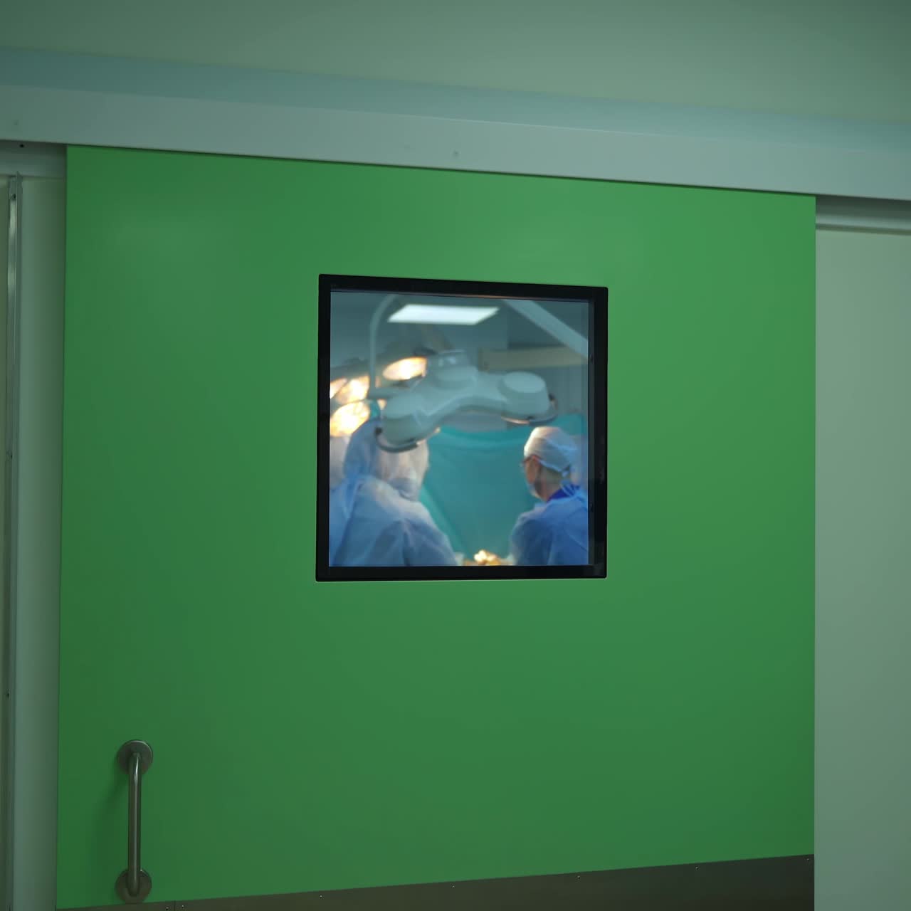 Operating process through the window in hospital. Teamwork of doctors perform an operation to a patient. Intensive care unit through the corridor window.