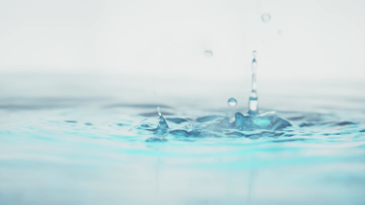 슬로우 모션의 깨끗한 물 표면은 물이 튀는 상점으로 화면을 채우고 기포로 액체 표면을 흔들고 있습니다.
