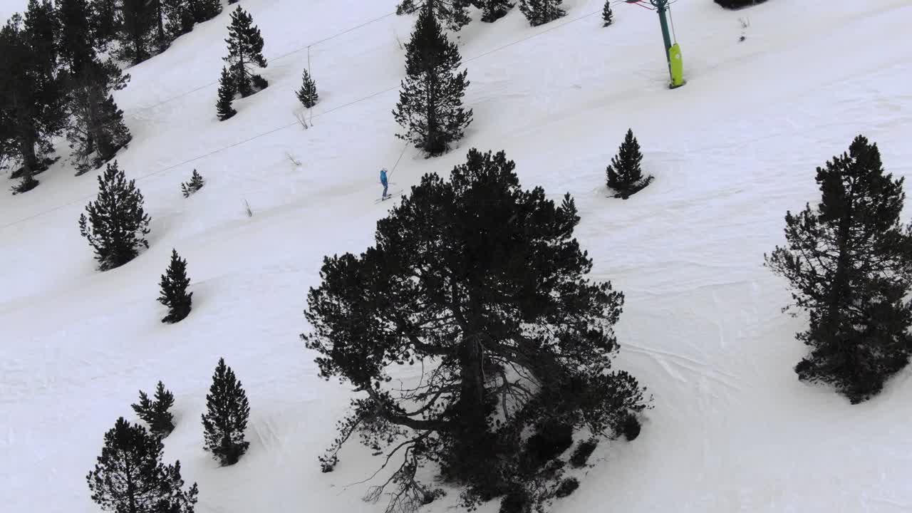 Aerial view of skier on snowy slope ascending mountain with skylift among pine trees, Ordino Arcalis ski resort, Andorra
