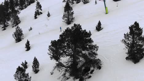 aerial view of skier on snowy slope ascending mountain with skylift among pine trees, ordino arcalis ski resort, andorra