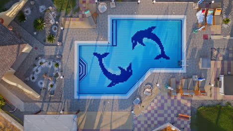 top down drone shot descending above a pool with dolphins, at a villa, sunrise