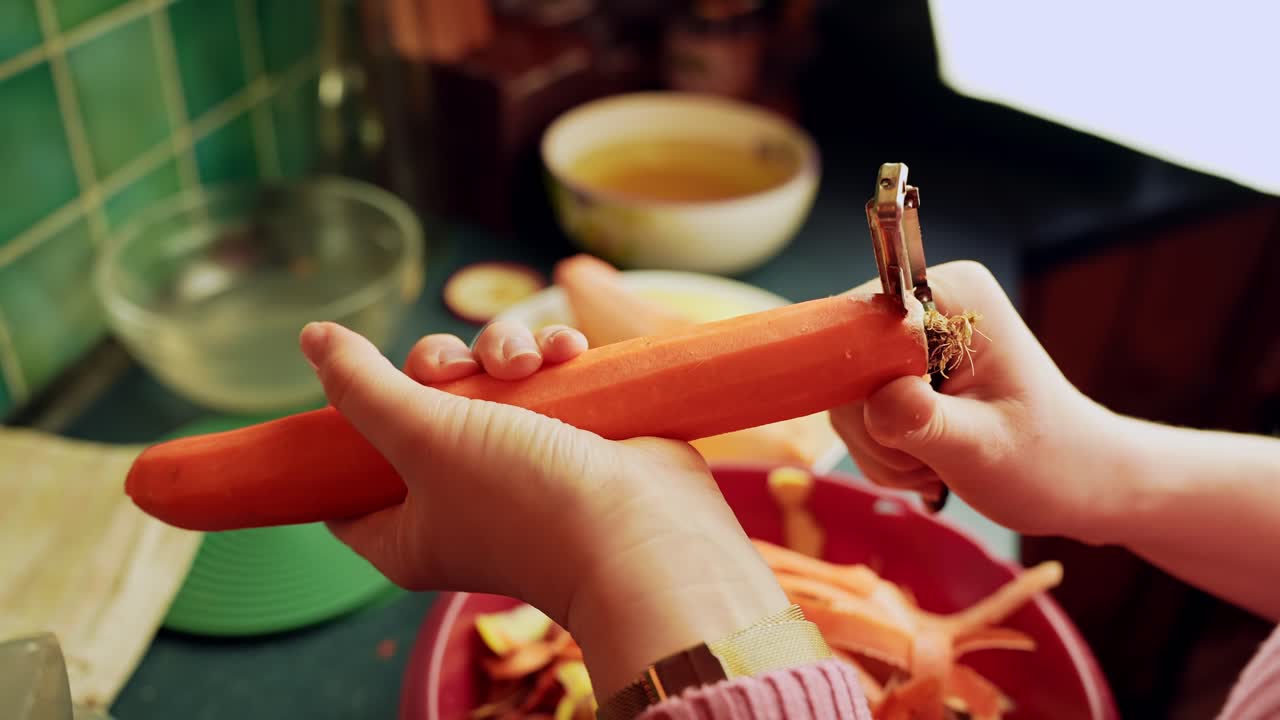 Primo piano di mani che sbucciano una carota con un pelaverdure sopra una ciotola sul bancone della cucina, preparando le verdure per la cena mentre un bambino guarda sullo sfondo