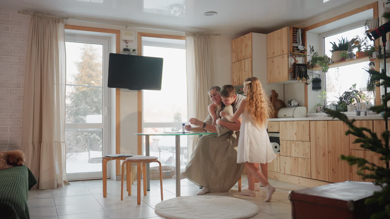 Woman in gown sitting on chair, crossing her legs while two children run toward her and happily hug her, background features cozy room with wooden furniture and large windows