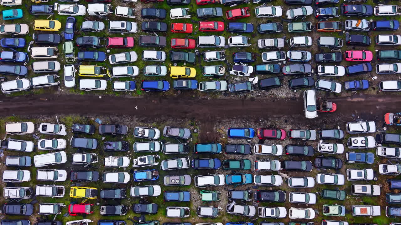 Auto's geparkeerd op een groot terrein op een schroothoop met verschillende kleuren en modellen overdag in een stedelijk gebied