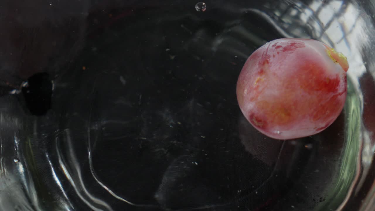Un singolo acino d'uva cade in un bicchiere d'acqua, creando increspature e bolle al rallentatore