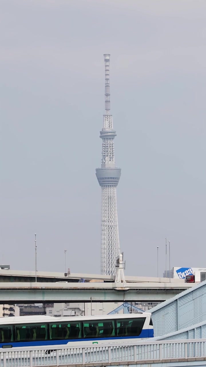Eine statische Teleaufnahme des Tokyo Skytree hinter einer Brücke mit fahrenden Fahrzeugen in Japan