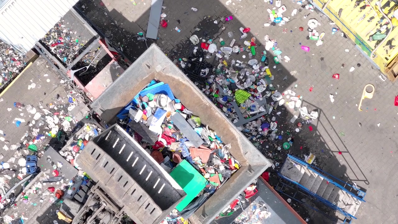 Camion scaricano rifiuti di plastica presso un impianto di riciclaggio. I lavoratori smistano i materiali per la lavorazione. I macchinari gestiscono la plastica per il recupero e lo smistamento. Le operazioni di gestione dei rifiuti supportano il riciclaggio.