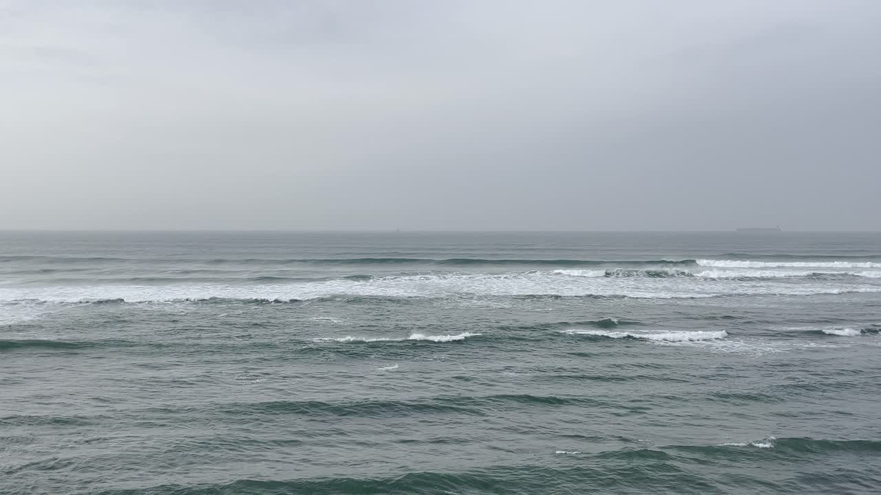 Peaceful scene of the Portuguese coastline, with gentle waves rolling over the ocean, creating a serene atmosphere. The muted sky and calm waters reflect the tranquil beauty of the seascape.