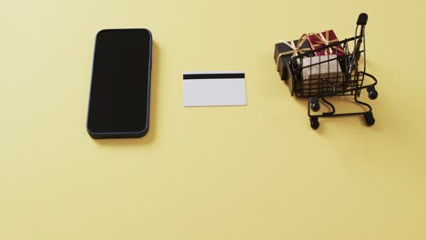 Video-Eines-Smartphones-Mit-Leerem-Bildschirm,-Kreditkarte,-Einkaufswagen-Auf-Gelbem-Hintergrund