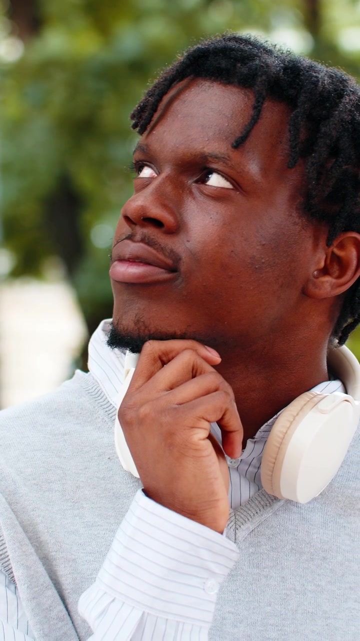 African american young man thinking with headphones walking in city street during quiet park visit