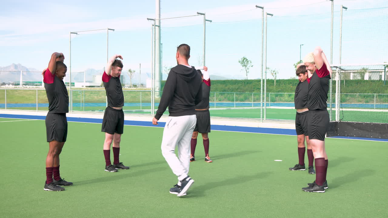 Coach leading male hockey team in stretching exercises on field