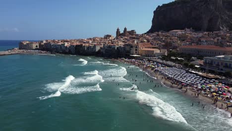 ocean fly-over a busy beach coastline with umbrellas and the city cathedral