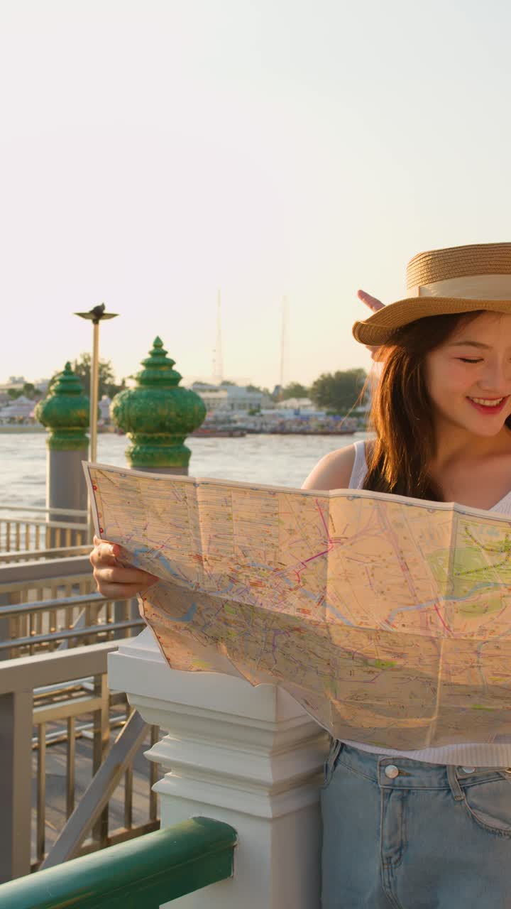 Coppia asiatica consulta una mappa vicino alla riva del Wat Arun, con luce dell'ora d'oro e un'atmosfera di viaggio rilassata