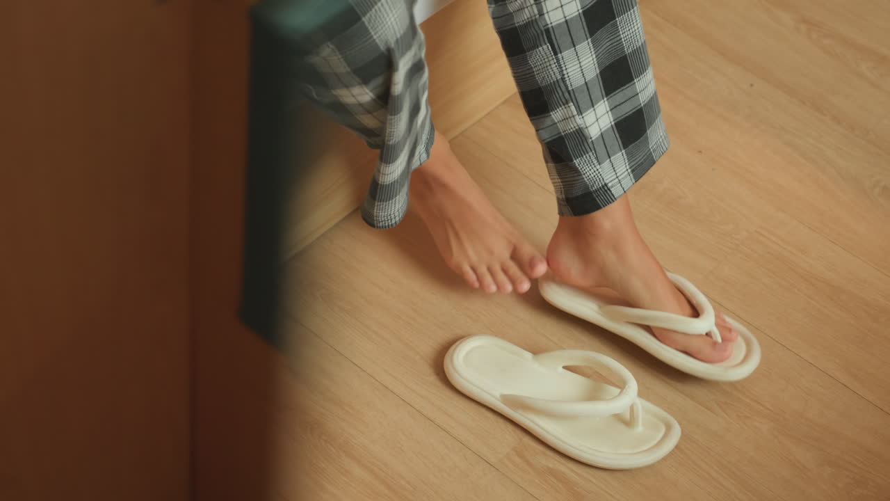Hotelværelsesdøråbning tomme tøfler efterladt på trægulvet, mens gæsten bevæger sig mod udgangen set gennem dørkarmen, stille aftenstemning, ensom afrejse og diskret bevægelse, ren parketstruktur og intim