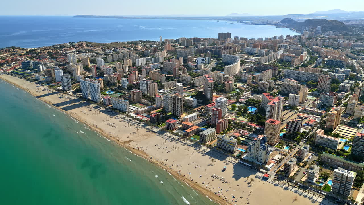 Aerial drone view of the buildings along the coastline with people relaxing on the beach in Alicante, Spain in daylight