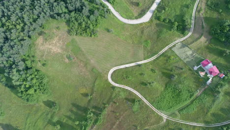 AERIAL:-Flying-arable-land,-with-a-forest-around-it-and-a-zigzag-road