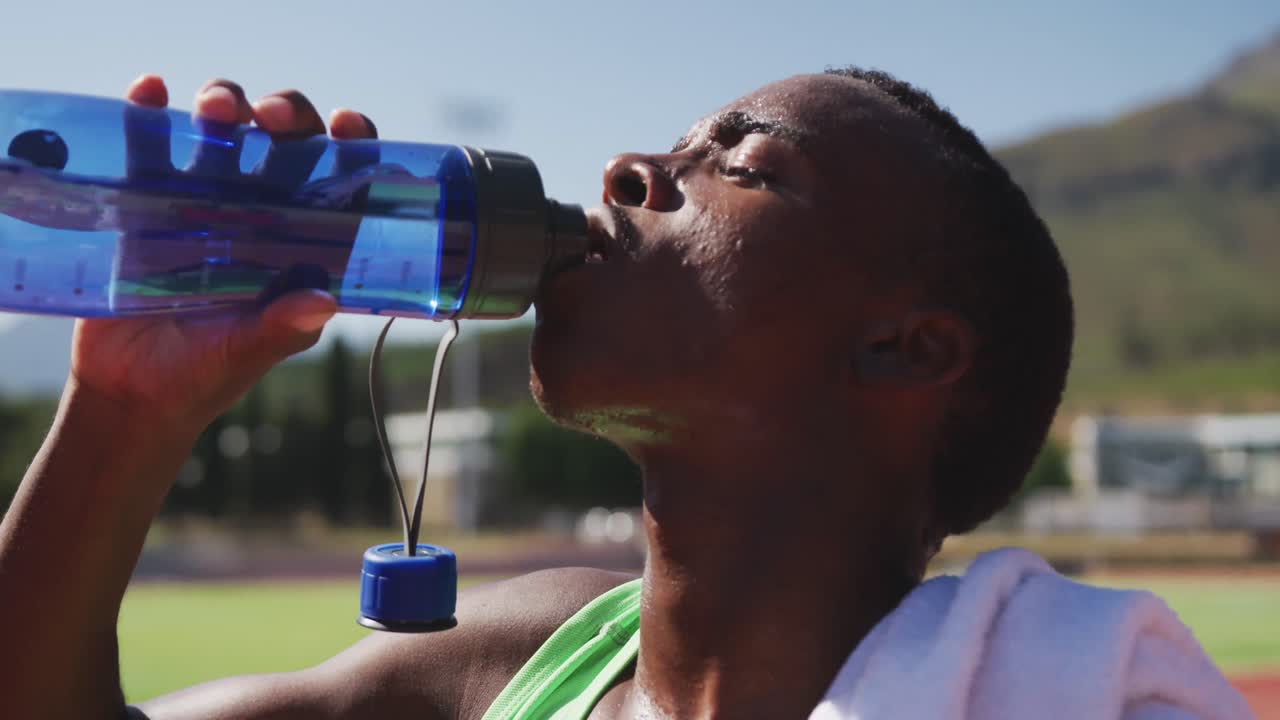 hombre de raza mixta discapacitado con piernas protésicas sentado en una pista de carreras y bebiendo agua