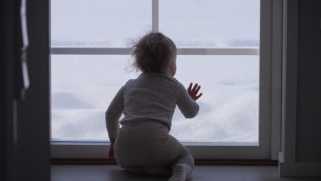 Young-Baby-Girl-Indoors-Looking-Out-at-Winter-Wonderland,-Santa-Christmas