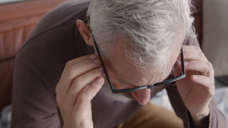 primer plano de un hombre de mediana edad que sufre con dolor de cabeza y toca sus sienes mientras se sienta en el sofá en casa 1