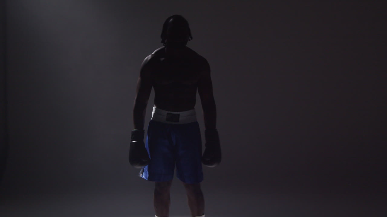 회색 배경에 빛의 풀에 서 있는 장갑을 입은 권투 선수의 낮은 키 조명으로 실루 스튜디오  1