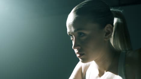 closeup from the side on a woman’s face and shoulders as she trains, with the camera gliding to the front. strong backlight creates dramatic highlights, capturing intensity and focus mid-workout