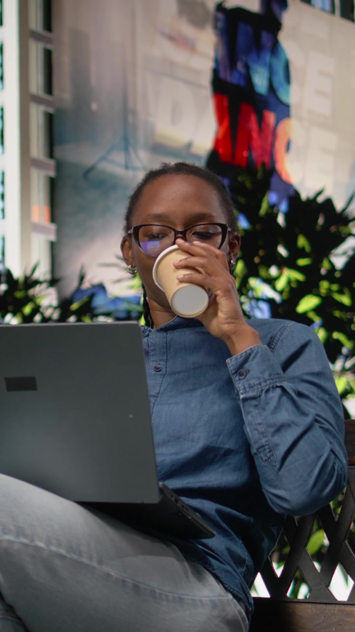 Vídeo Vertical Trabalhador remoto tomando café, usando notebook em banco no parque