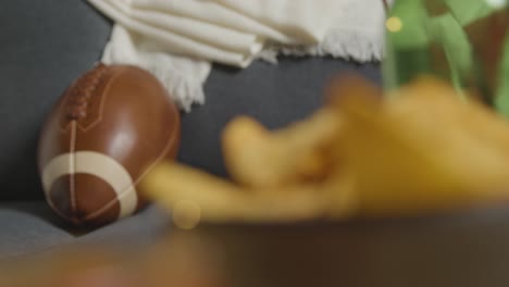 lounge at home of person watching american football game on tv with drinks snacks and ball 2