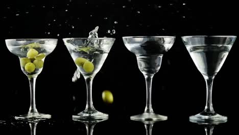 Grey-paper-burning-over-olives-falling-into-cocktail-glasses-against-black-background