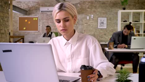 young happy businesswoman is typing on laptop in office, drinking coffee, colleagues are networking with technologies, work concept, communication concept