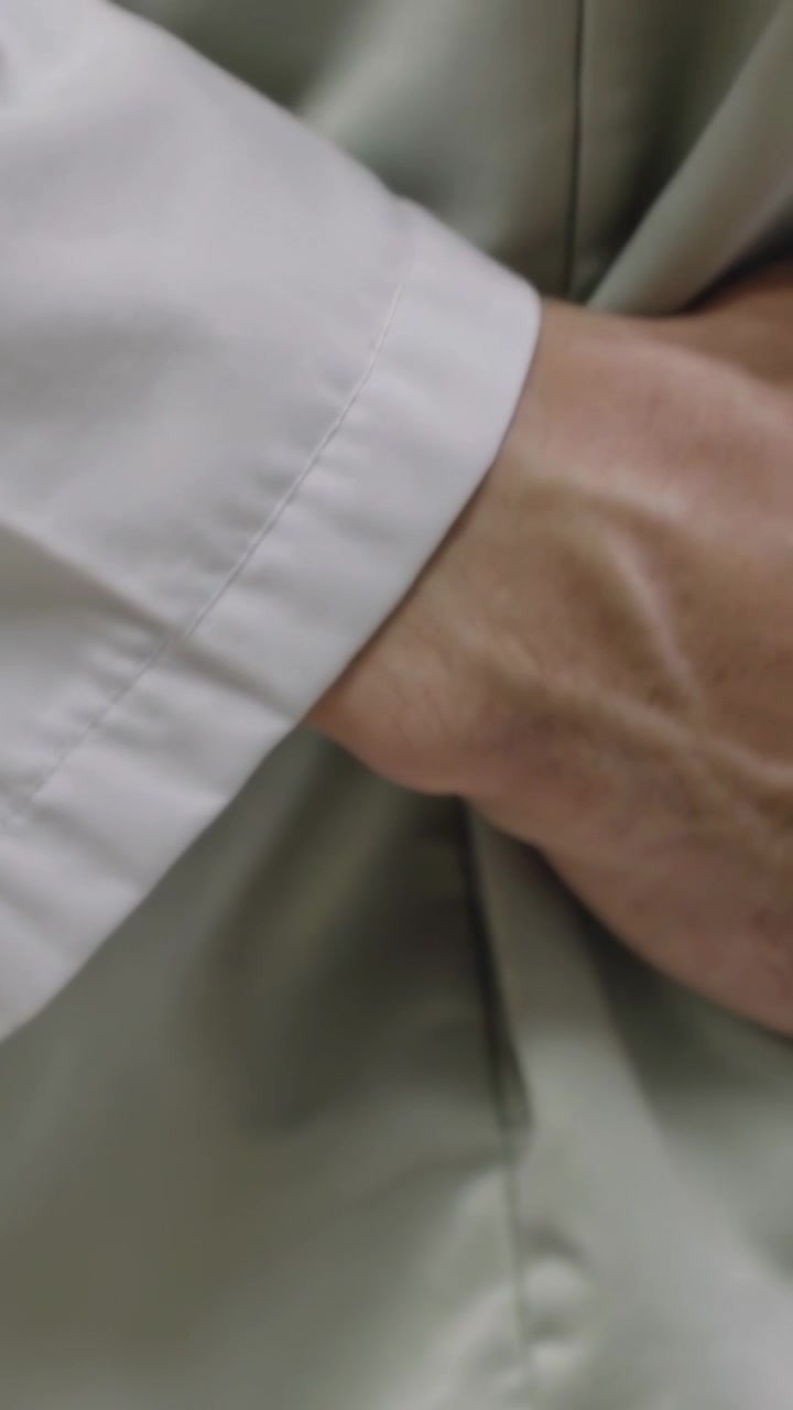 Video verticale: Mano venosa che si allunga per sostenere una persona in clinica, polsino bianco che preme su una camicia beige.