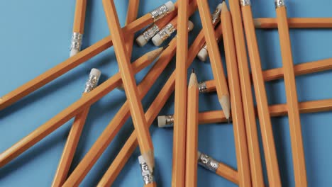 Overhead-view-of-scattered-pencils-with-blue-background,-in-slow-motion