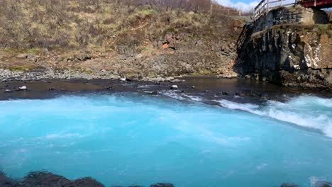filming from the bottom of the amazing waterfall bruarfoss with the most intense blue and turquoise water in iceland, showing the water pouring down from the small stones