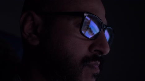 asian male reading with reflection of computer screens seen in glasses in dark room