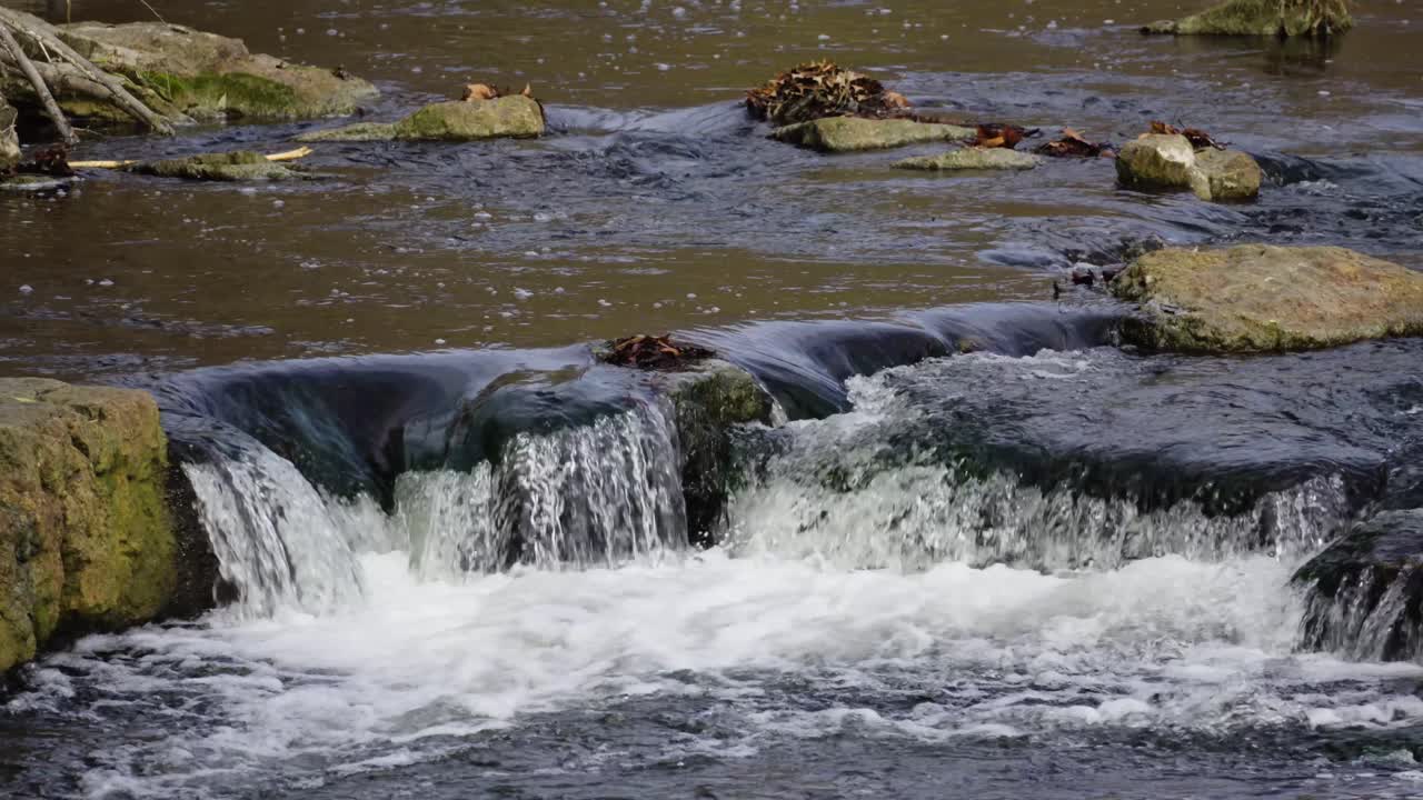 Multiple shallow mini waterfalls flowing and cascading down levels into rocky river