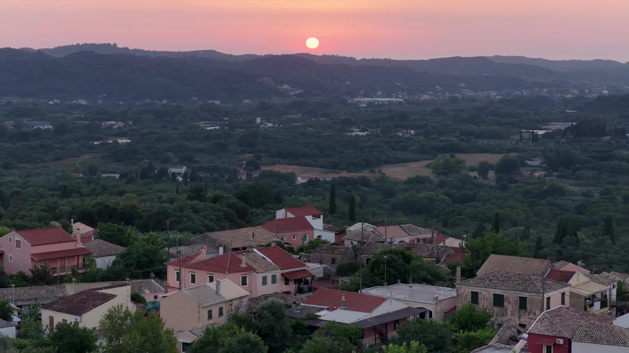 Panoramica aerea di case con tetto rosso e valle verde al tramonto ad Agioi Douloi, Corfù settentrionale, Grecia.