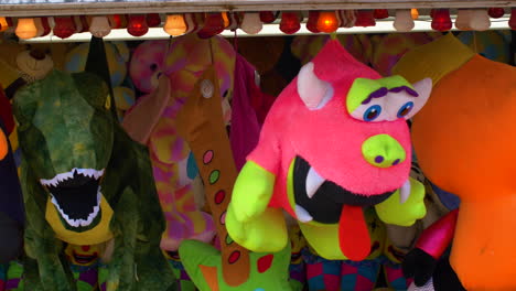 pinkie and dinosaur stuffed animals hang on display at a carnival above the game station