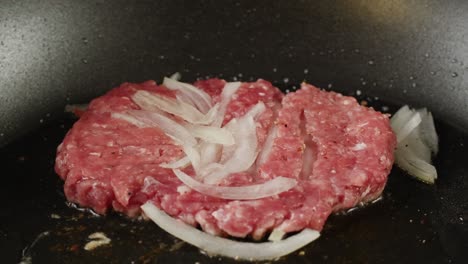 cooking a raw hamburger patty with onions in a pan