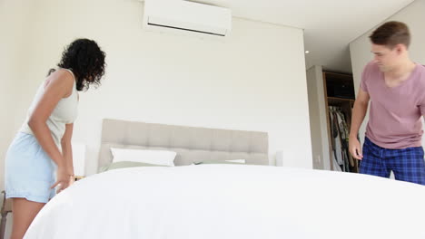 making bed together, young multiracial couple arranging pillows in modern bedroom, at home